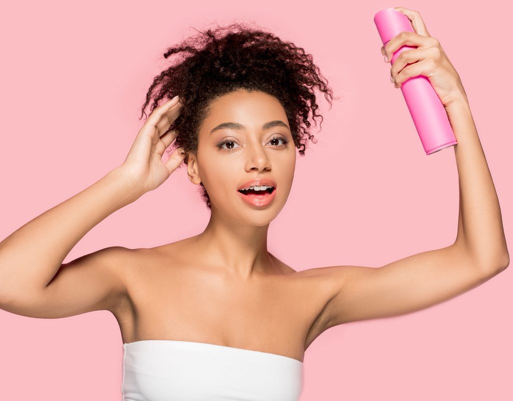 A woman spraying her hair with product.