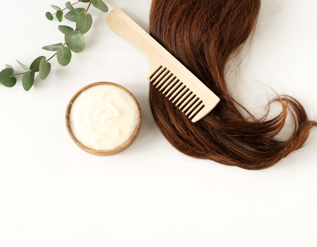 A hair mask, comb, and hair on a white background.