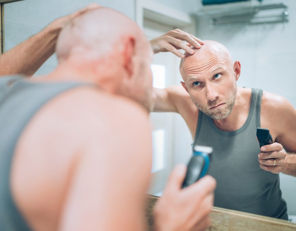A man checking his shaved head in the mirror.