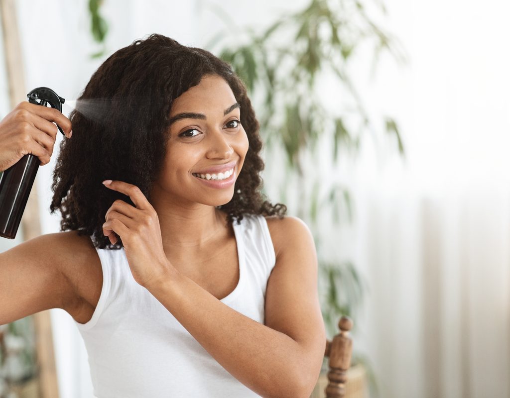 A Black woman spraying product in her hair.