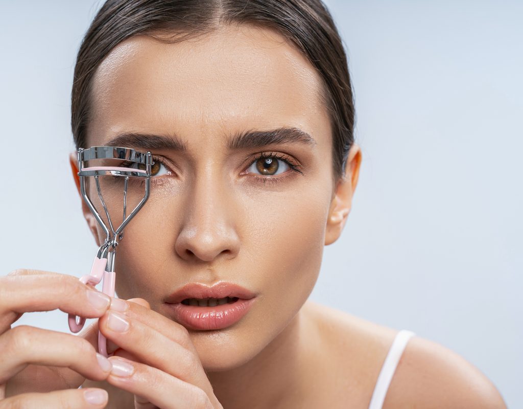 A woman curling her eyelashes.