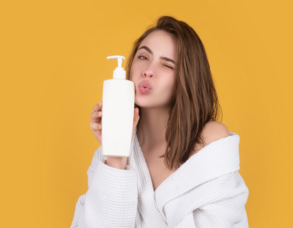A woman holding up a hair care product to her face.