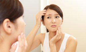 A woman looking at her face in a mirror.