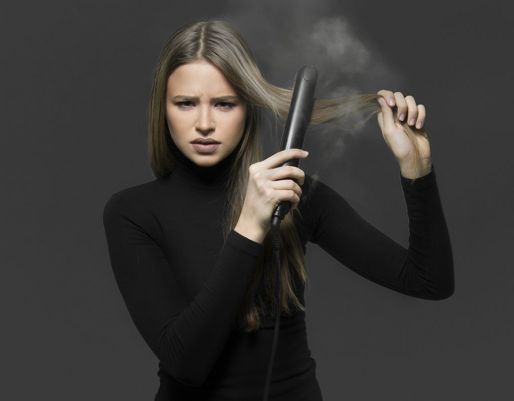 A woman taking a flat iron to her hair and smoke coming out of it.