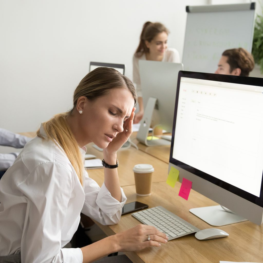 Woman in office grabbing head while working at computer