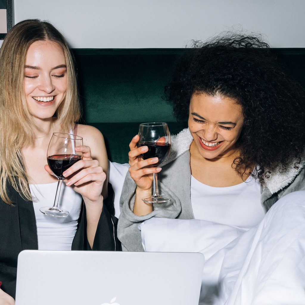 Two women watching tv in bed with wine