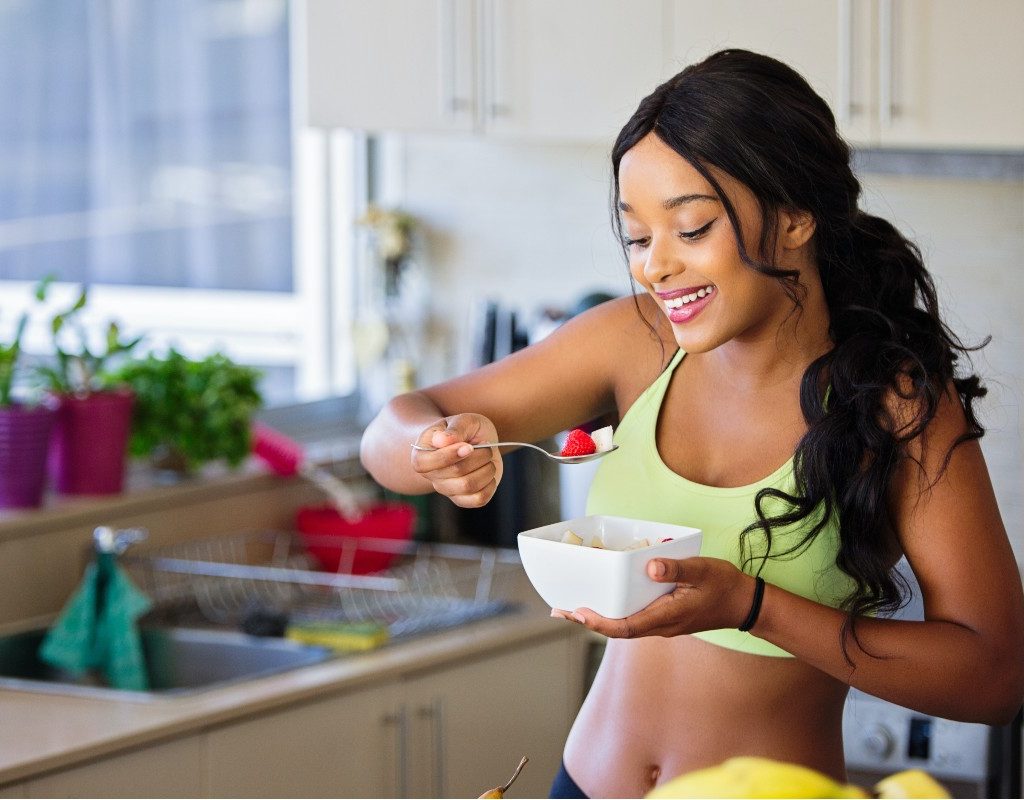 a woman eating a strawberry with a spoon while holding a white bowl