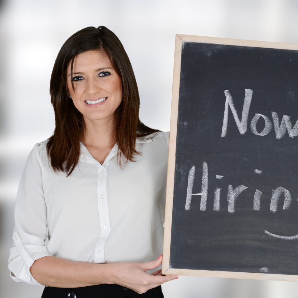 Woman holding chalkboard sign that says "Now Hiring"