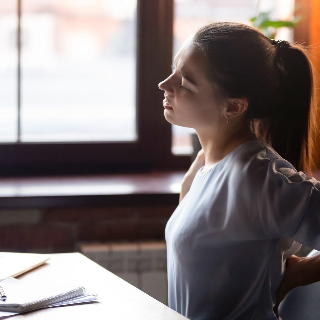 Woman grabbing back in pain while at computer
