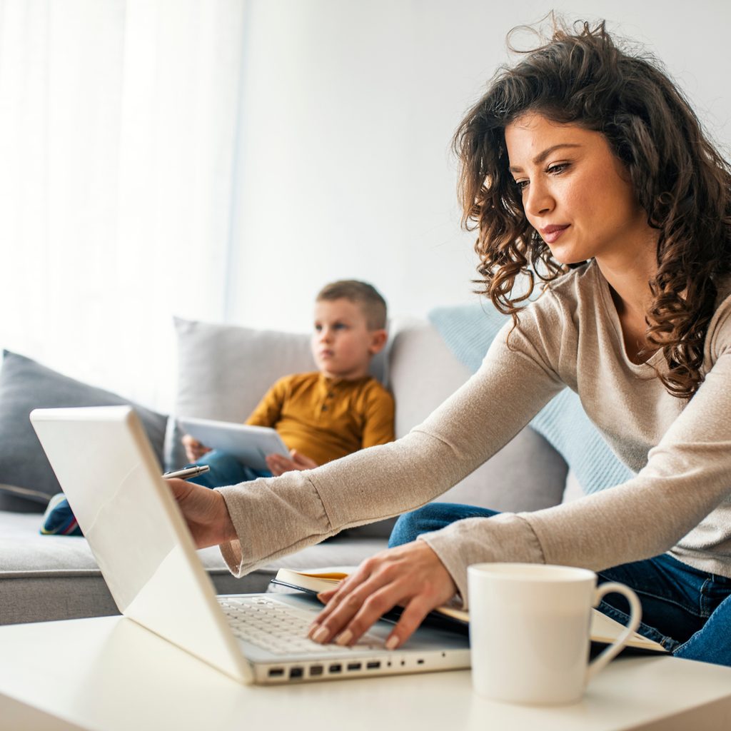 Woman sitting on couch working on laptop hunched over coffee table