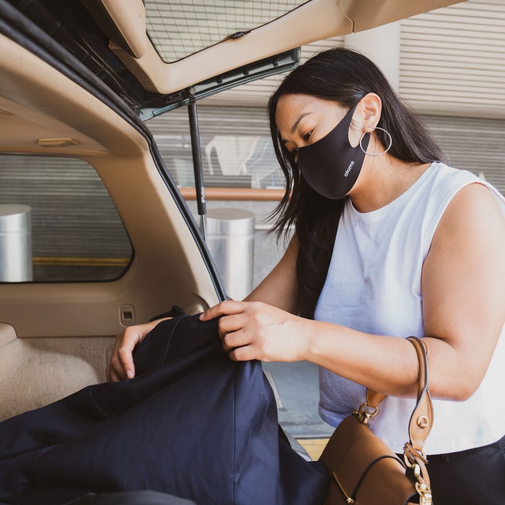 woman at airport unloading suitcase from car while wearing a mask