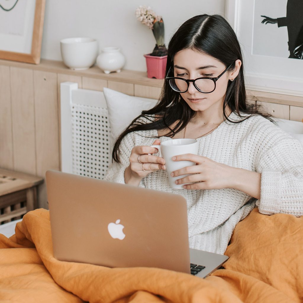 Woman using her laptop in bed with a mug