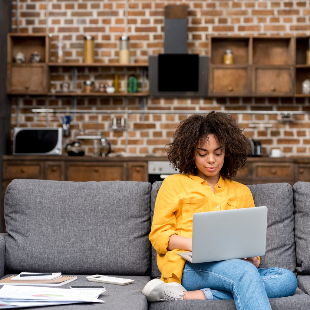 woman working while sitting on couch with laptop on lap
