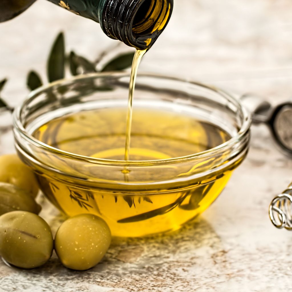 Olive oil pouring into a bowl with olives