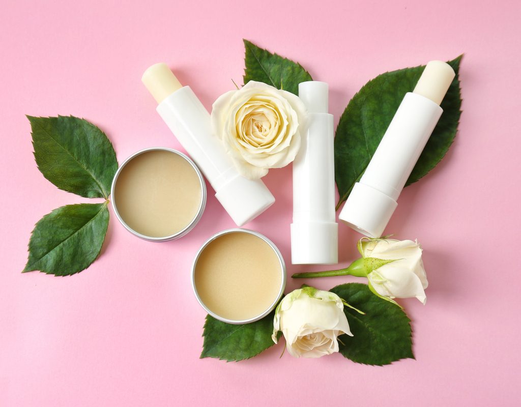 A variety of lip balms and leaves and flowers on a table.