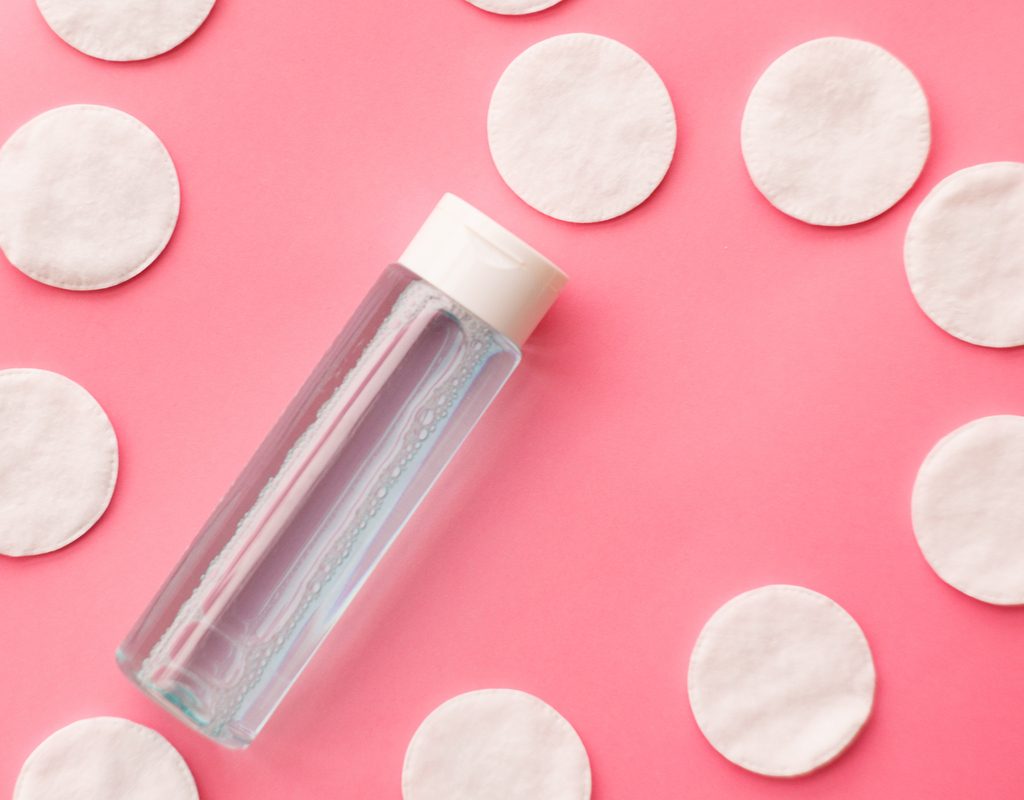 Face toner and cotton pads on a pink background.