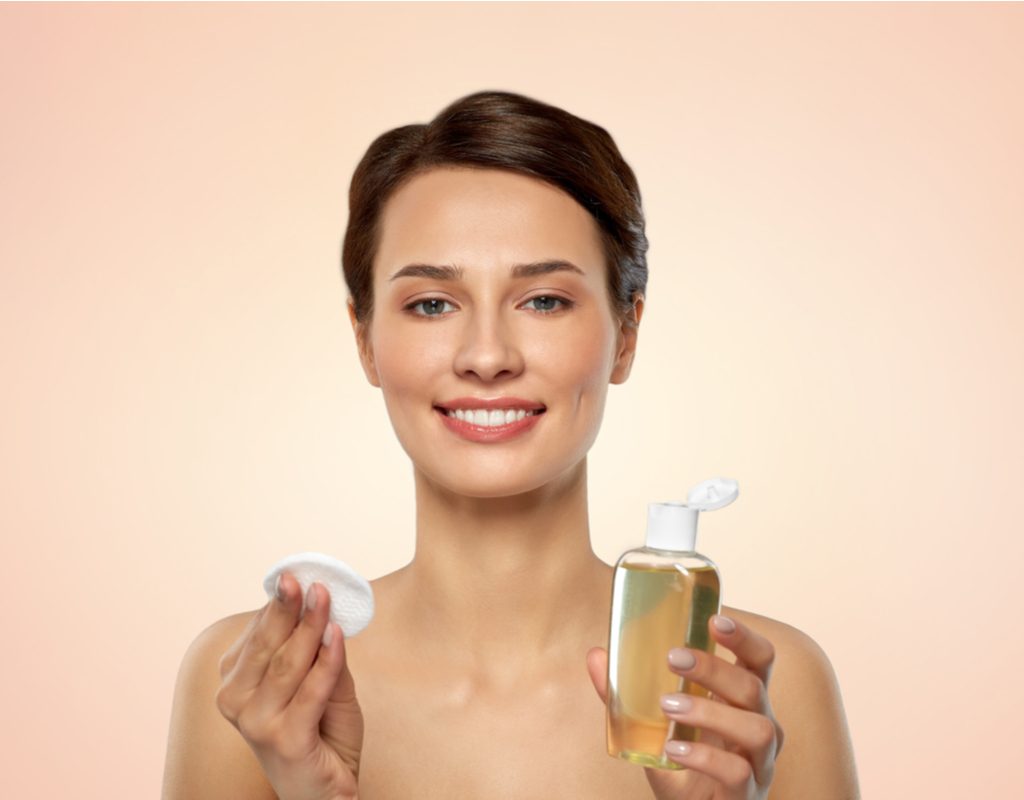 A woman holding up face toner and cotton pads.
