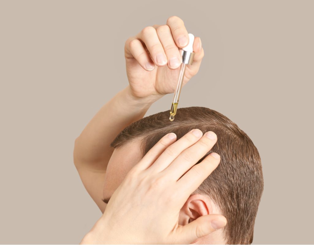 A man putting hair oil on his hairline.