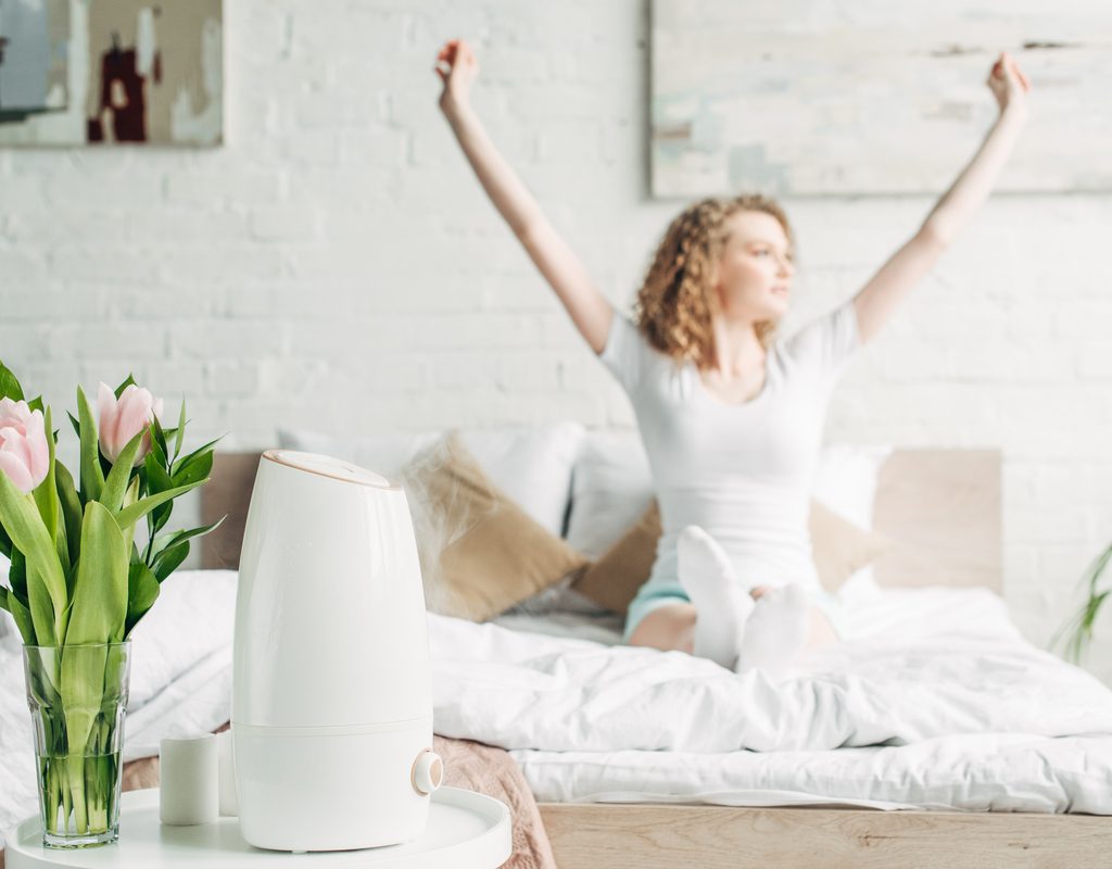 A woman waking up with an air purifier in her room.