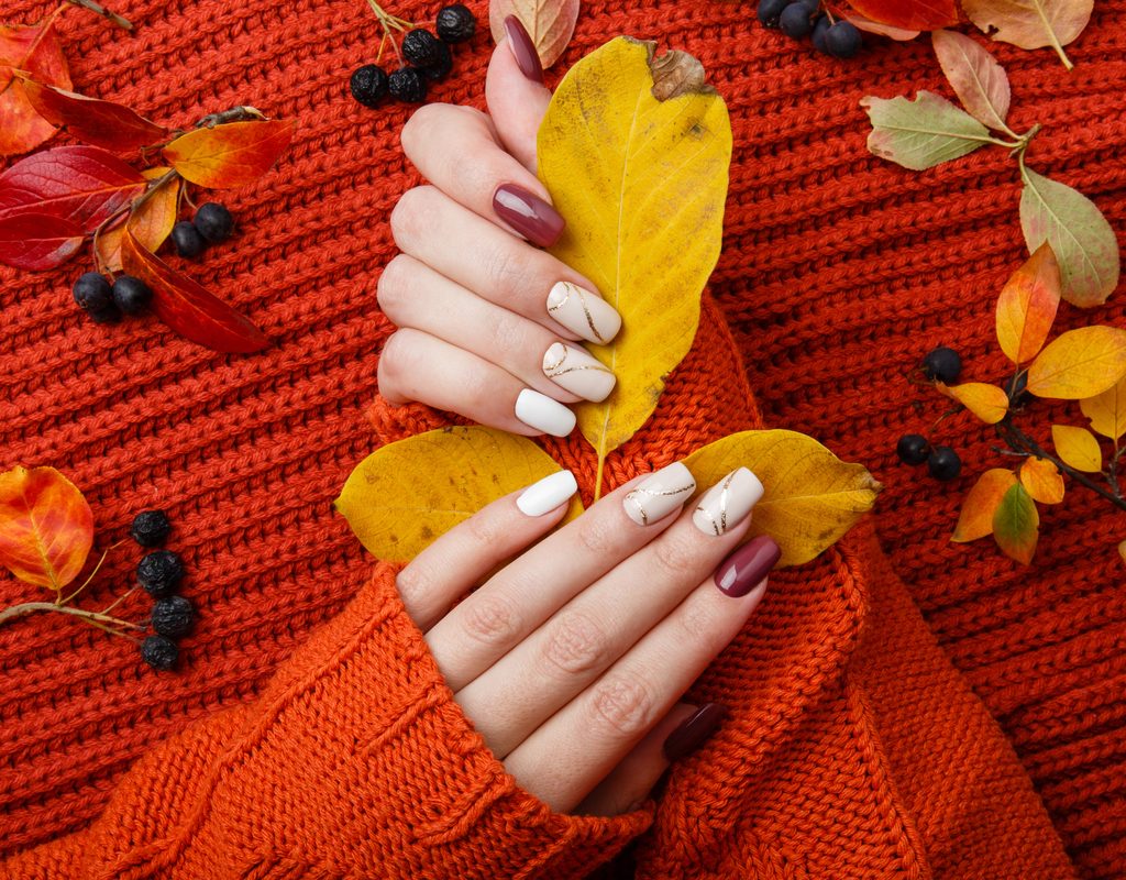 Fall-themed nails, leaves, and an orange sweater background.