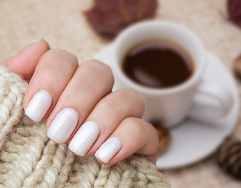 White painted nails with a coffee and leaves in the background.
