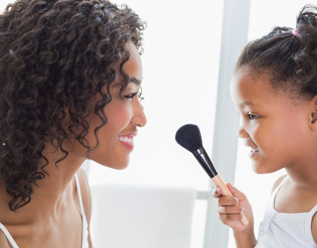 A mother letting her daughter put makeup on her face.