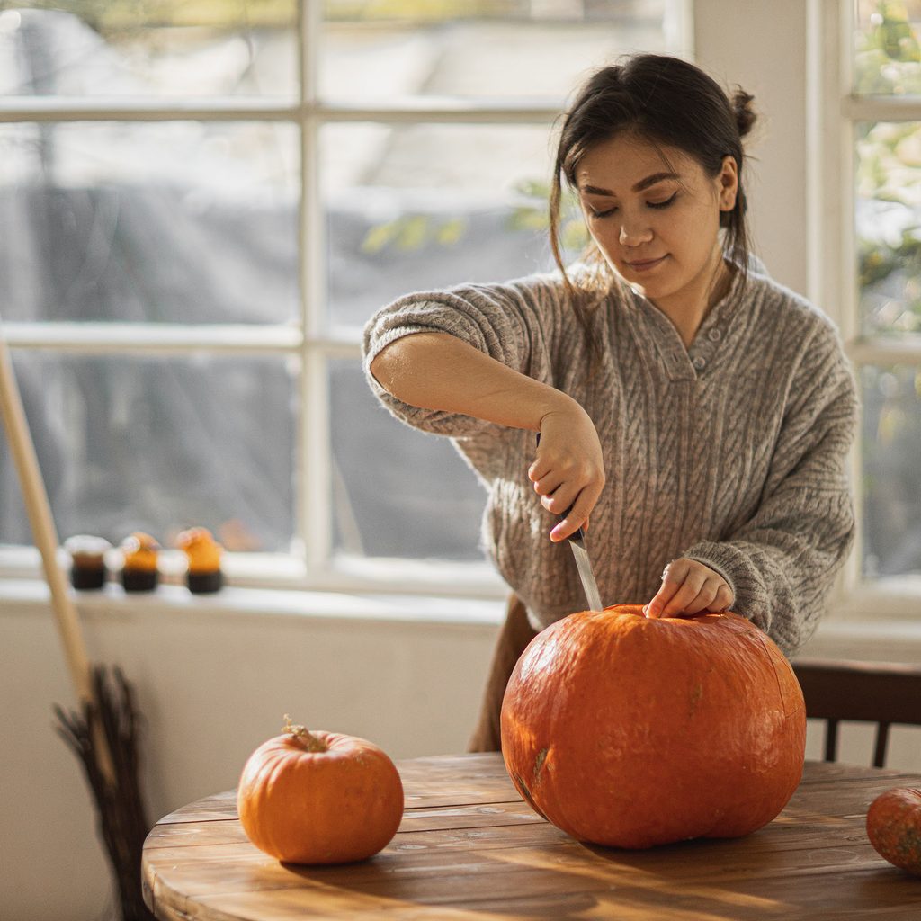 Woman cutting the top off of a pumpkin
