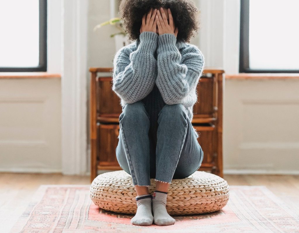 a woman sitting on a pillow with her hands over her face