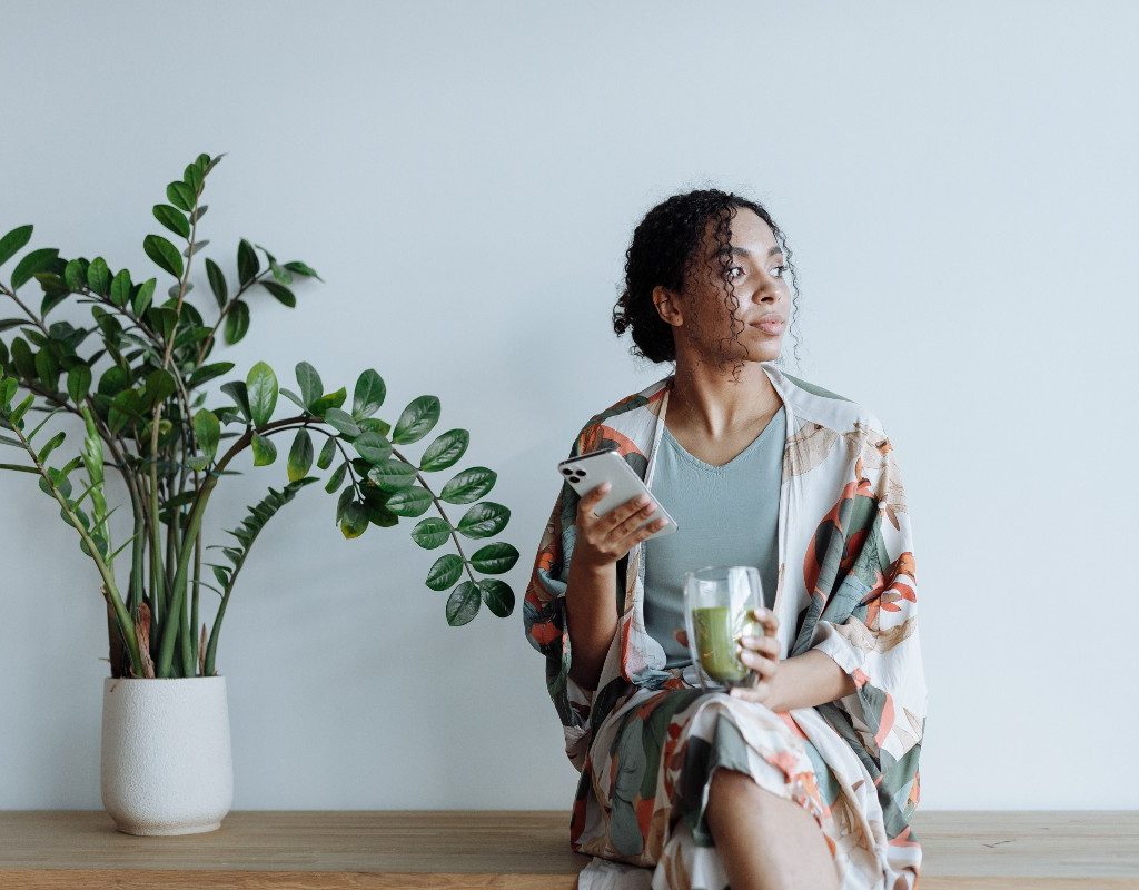 woman holding green juice in one hand and a phone in the other