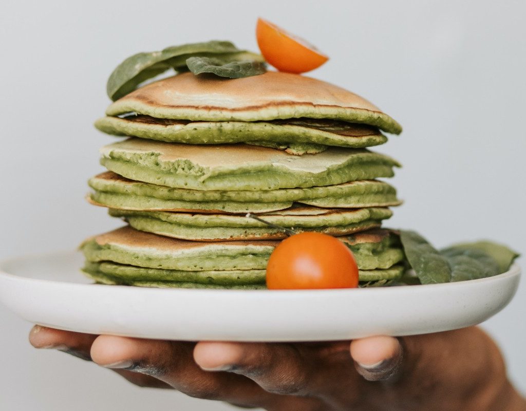a stack of zucchini pancakes on a white plate with tomato garnish