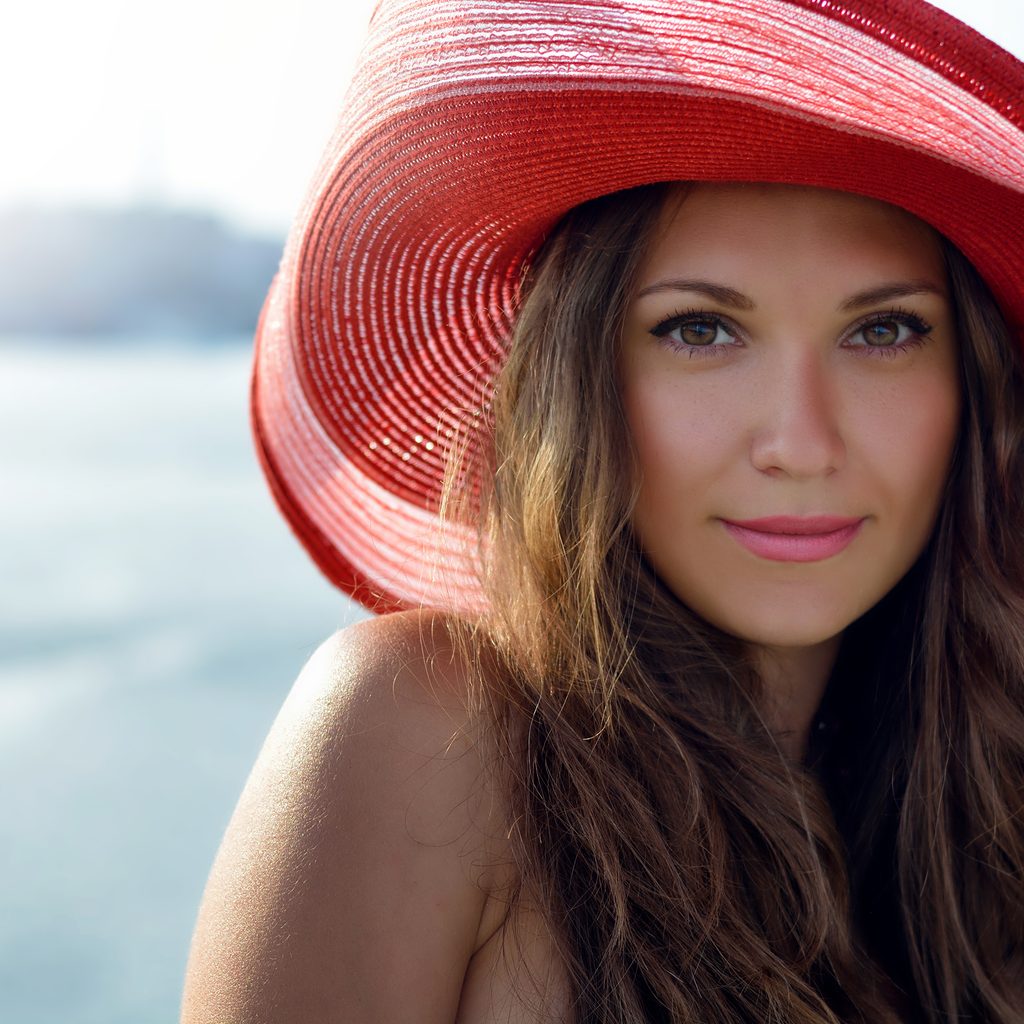 close up of woman wearing a red hat with beach in background