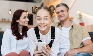 A young teen on her phone with her parents in the background.
