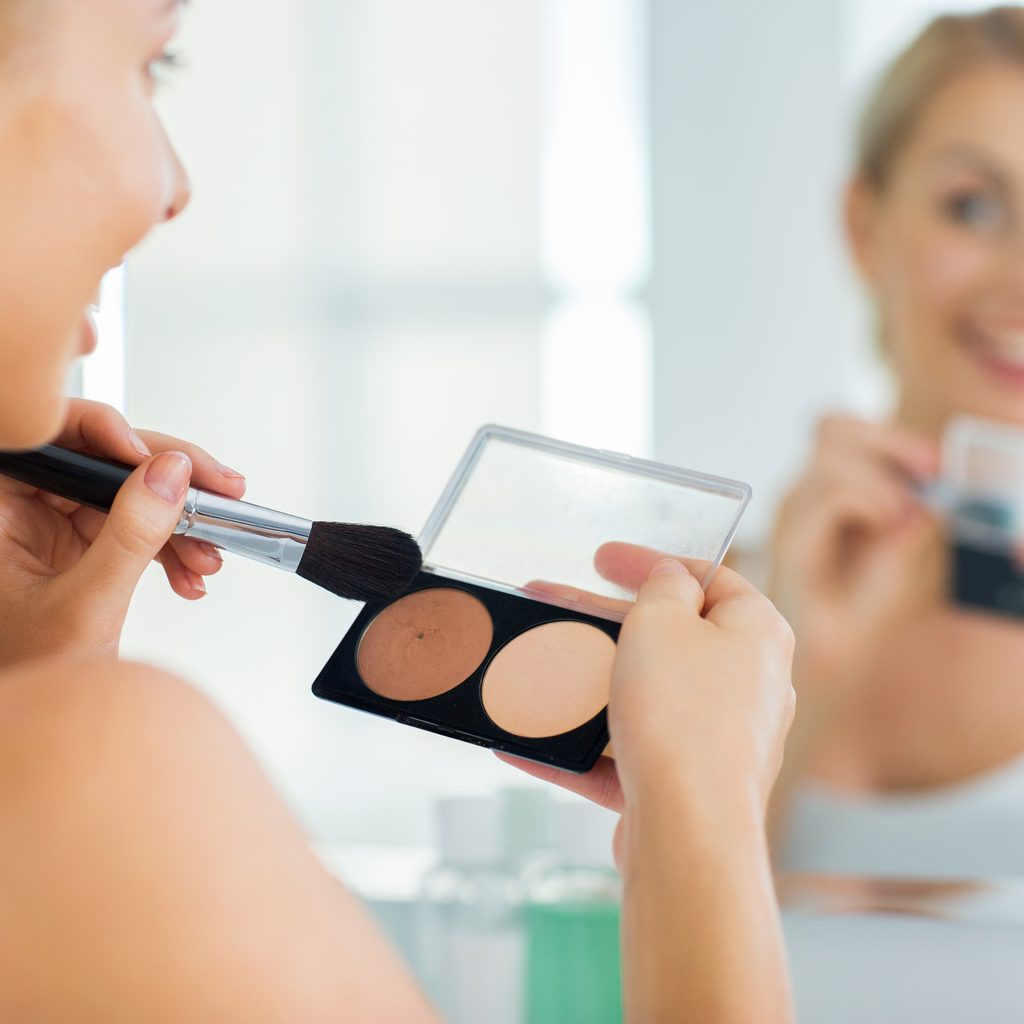 woman looking in mirror applying highlighter with brush