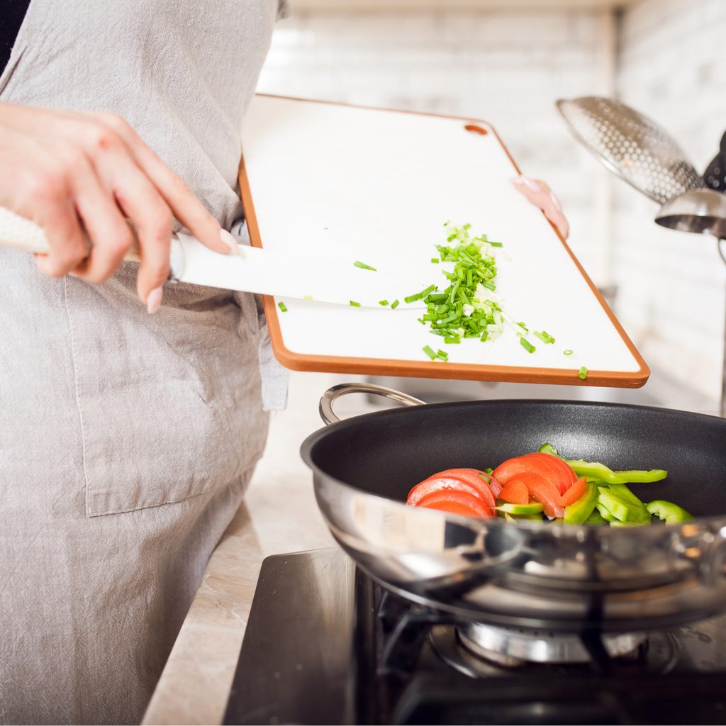 Closeup of woman's hands putting vegetables in pan