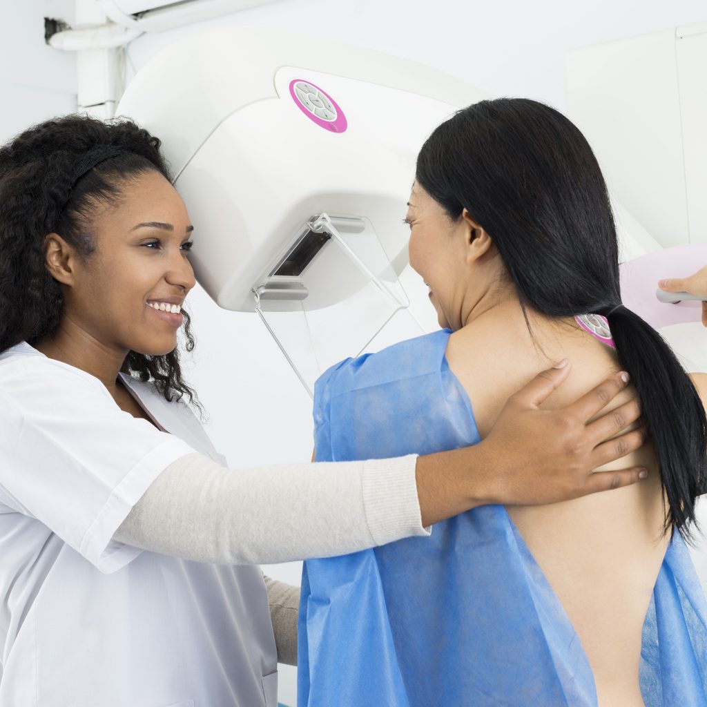smiling woman undergoing mammogram with technician