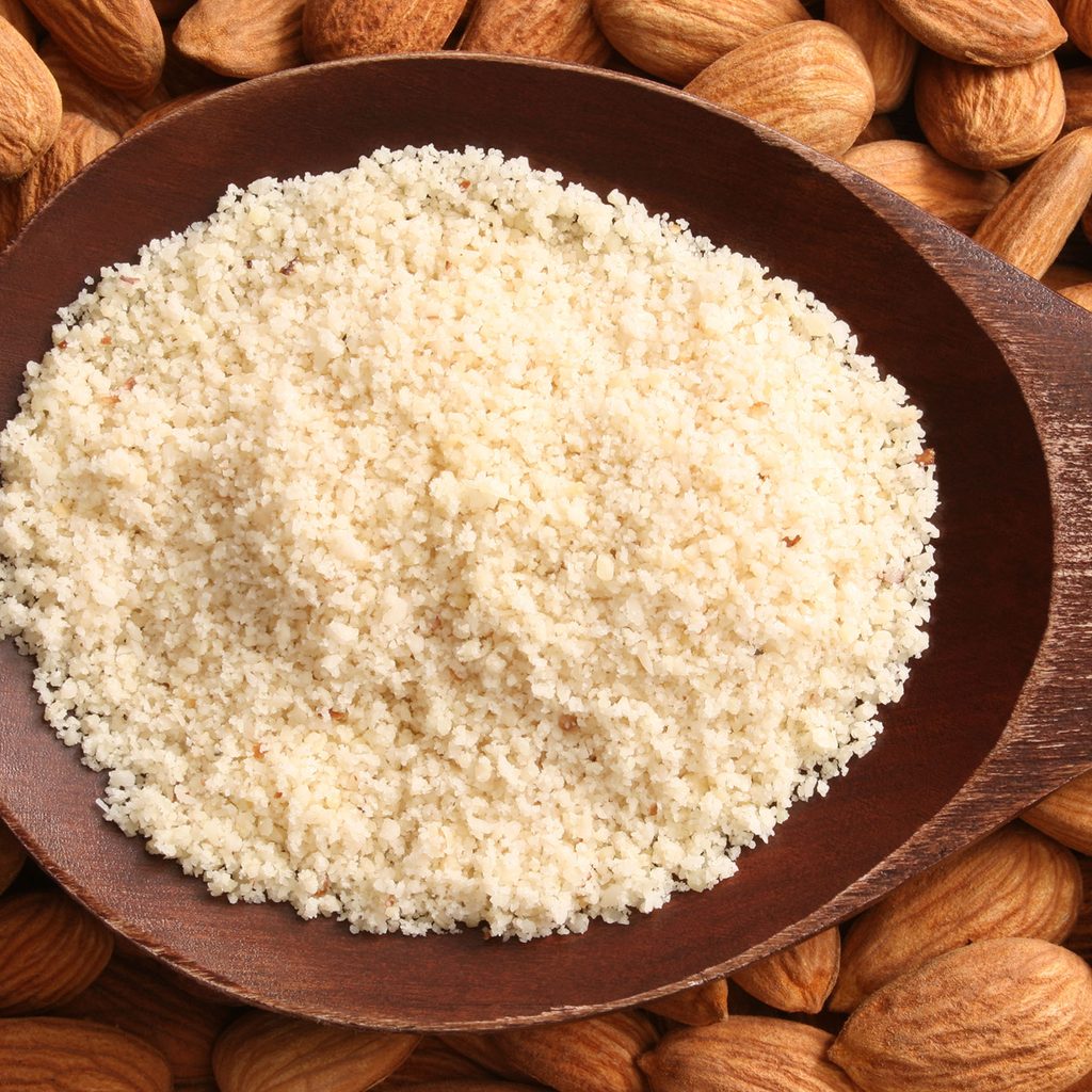 Almond flour on a spoon surrounded by almonds