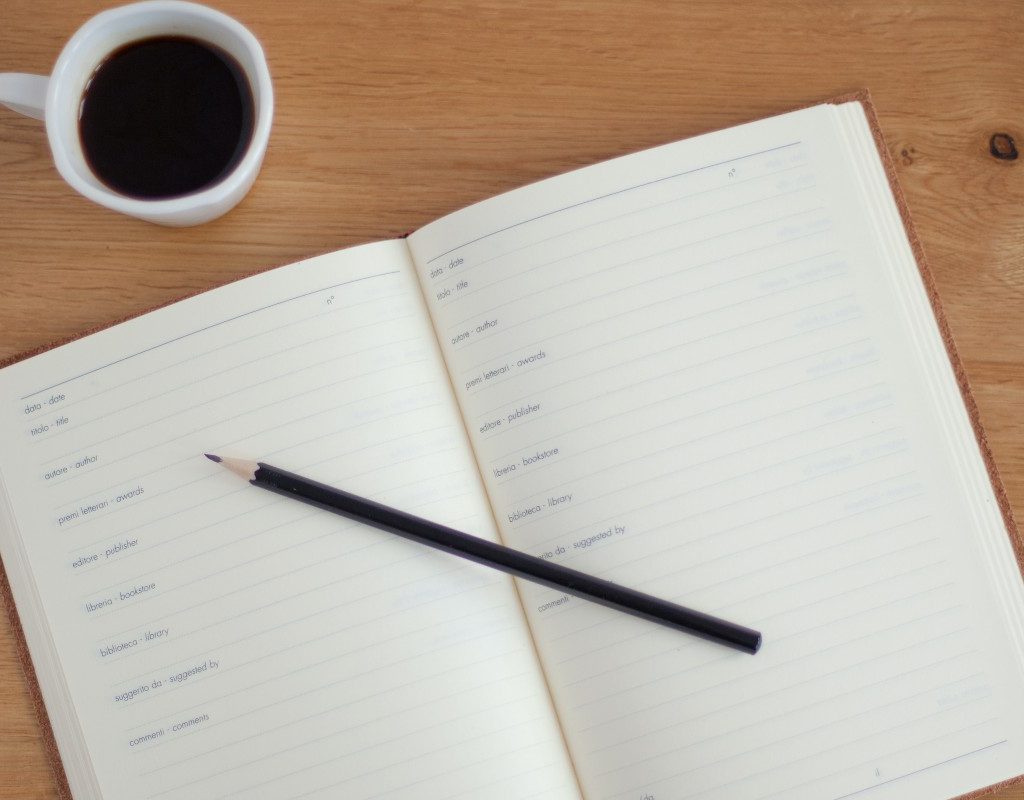 a journal, pencil, and coffee on a desk