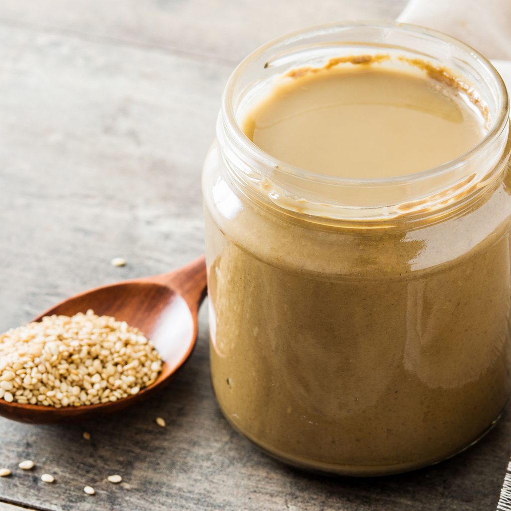 Jar of tahini and a spoonful of sesame seeds