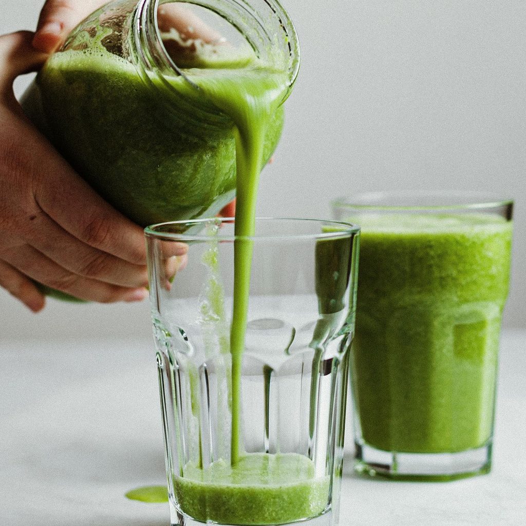 Person pouring green smoothie into cups