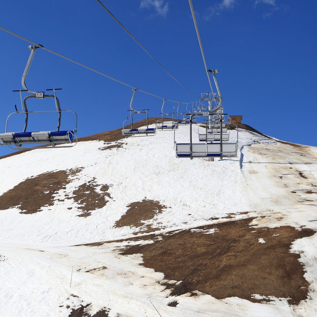 Empty skilifts over a hill with grass coming through the snow