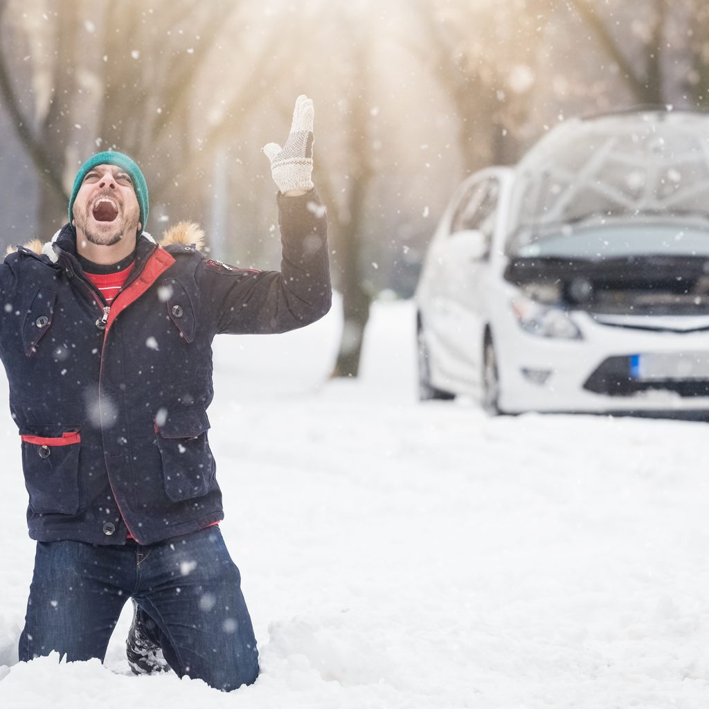Man on knees in snowdrift screaming in front of a stalled car