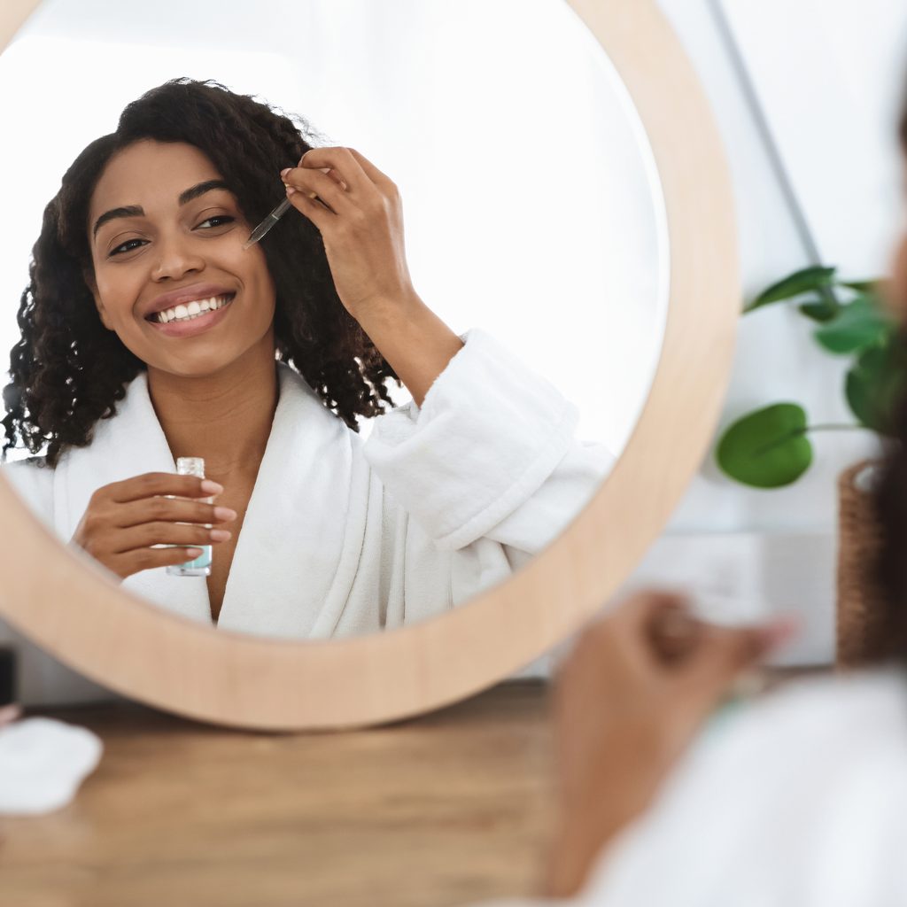 Woman looking in mirror applying facial oil