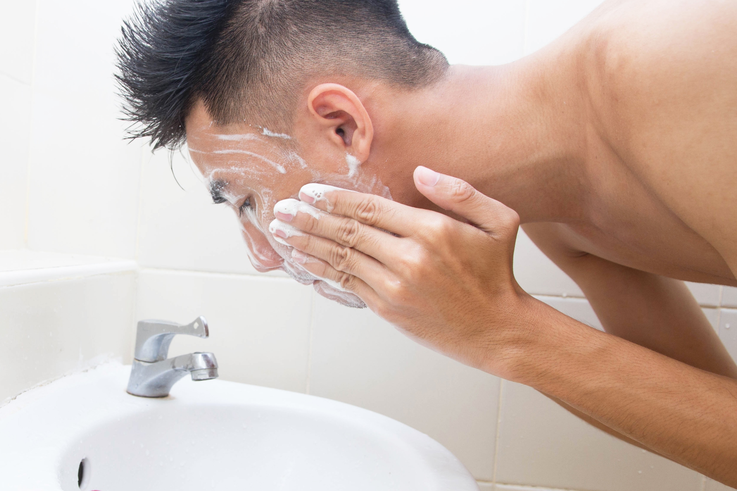 young man cleansing face in sink