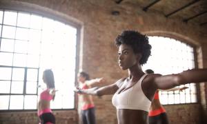 Young Black woman doing yoga with her arms raised.