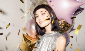 Girl with baby bangs surrounded by confetti and balloons.