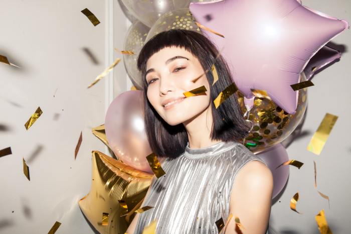 Girl with baby bangs surrounded by confetti and balloons.