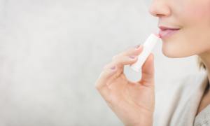A woman applying pink lip balm.