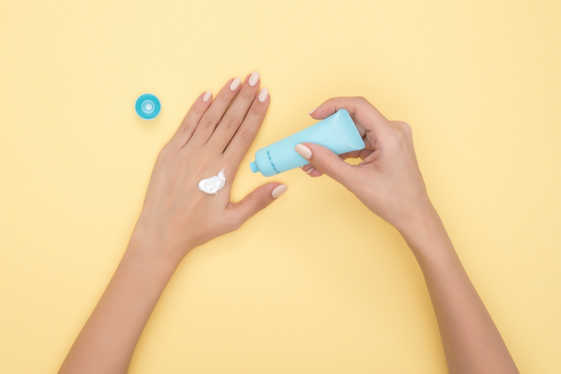 A woman applying sunscreen from a tube with a yellow background.