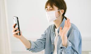 A masked woman making a video call on her phone.