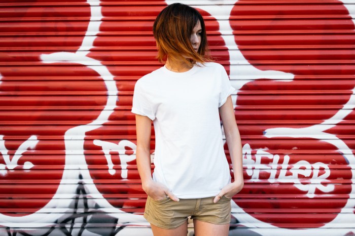 a young girl with short dark hair wears a white t shirt and khaki shorts in front of a red graffiti wall
